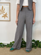 Person wearing gray wide-leg pants with a white top and green shoes, standing indoors.