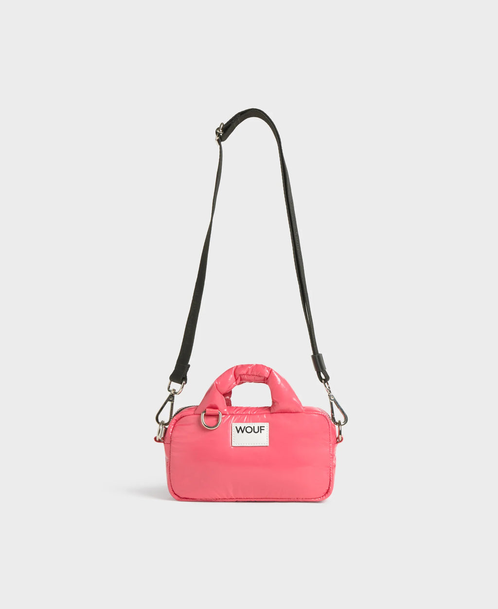Pink dog carrier with a black strap on a light gray background
