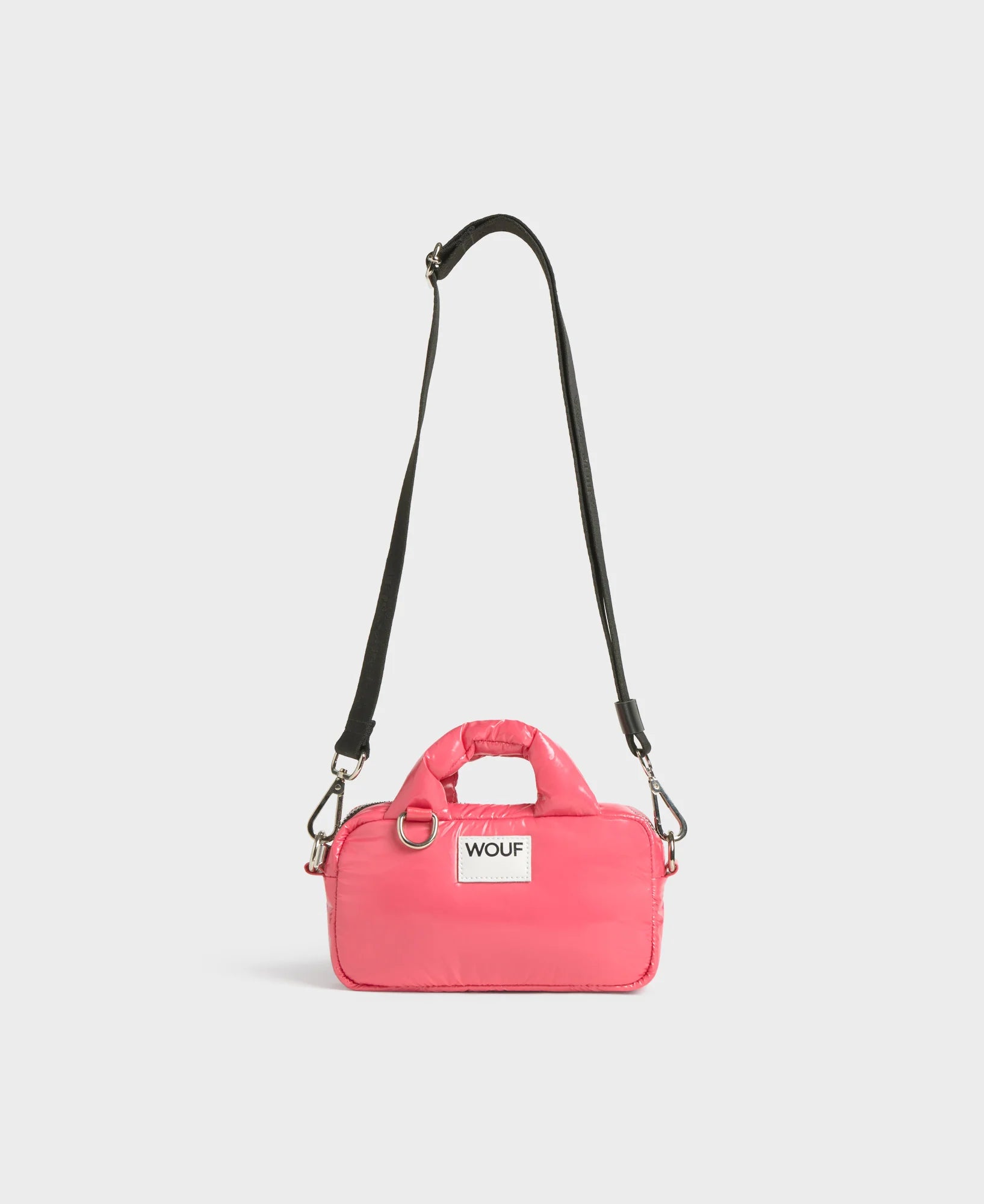 Pink dog carrier with a black strap on a light gray background