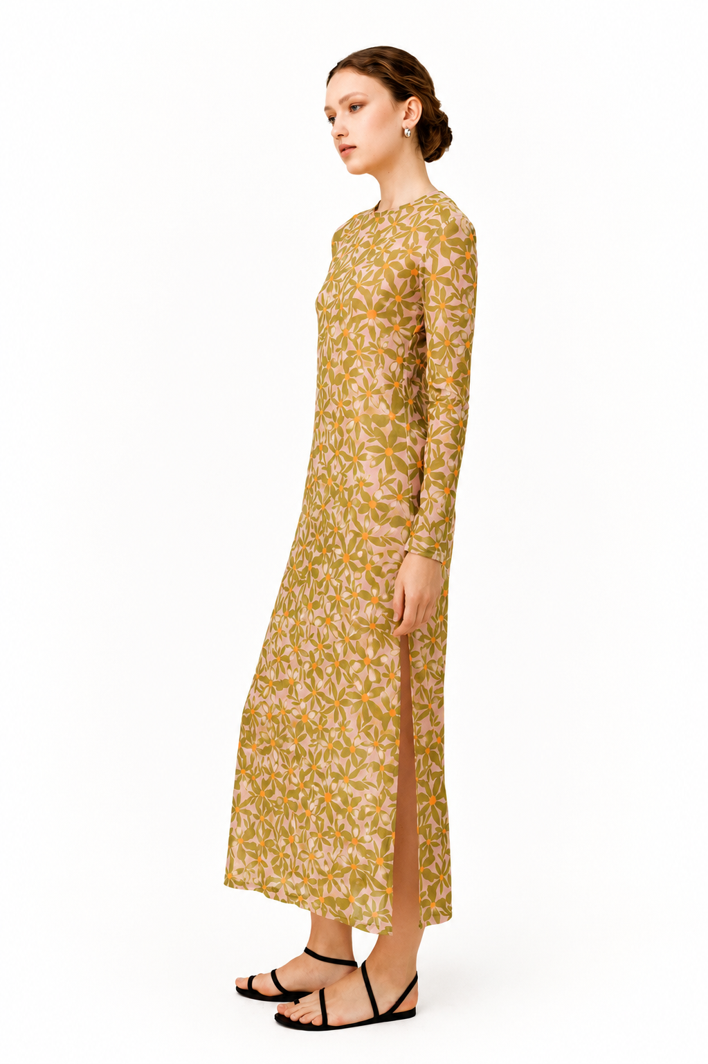 A woman modeling a long-sleeved maxi dress with a beige and olive green floral pattern, standing in profile against a plain white background.