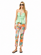 A woman modeling a light green halter crop top and bright orange tropical print pants against a plain white background.