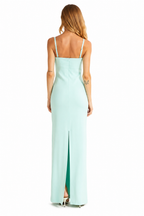 A woman viewed from the back wearing a mint green sleeveless maxi dress with thin straps and a front slit, standing against a plain white background.