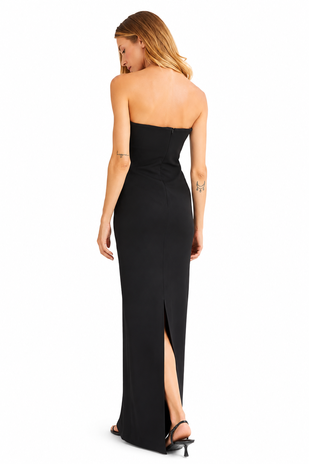A woman modeling a strapless black maxi dress from the back, featuring a fitted silhouette, a high slit, and black strappy heels against a plain white background.