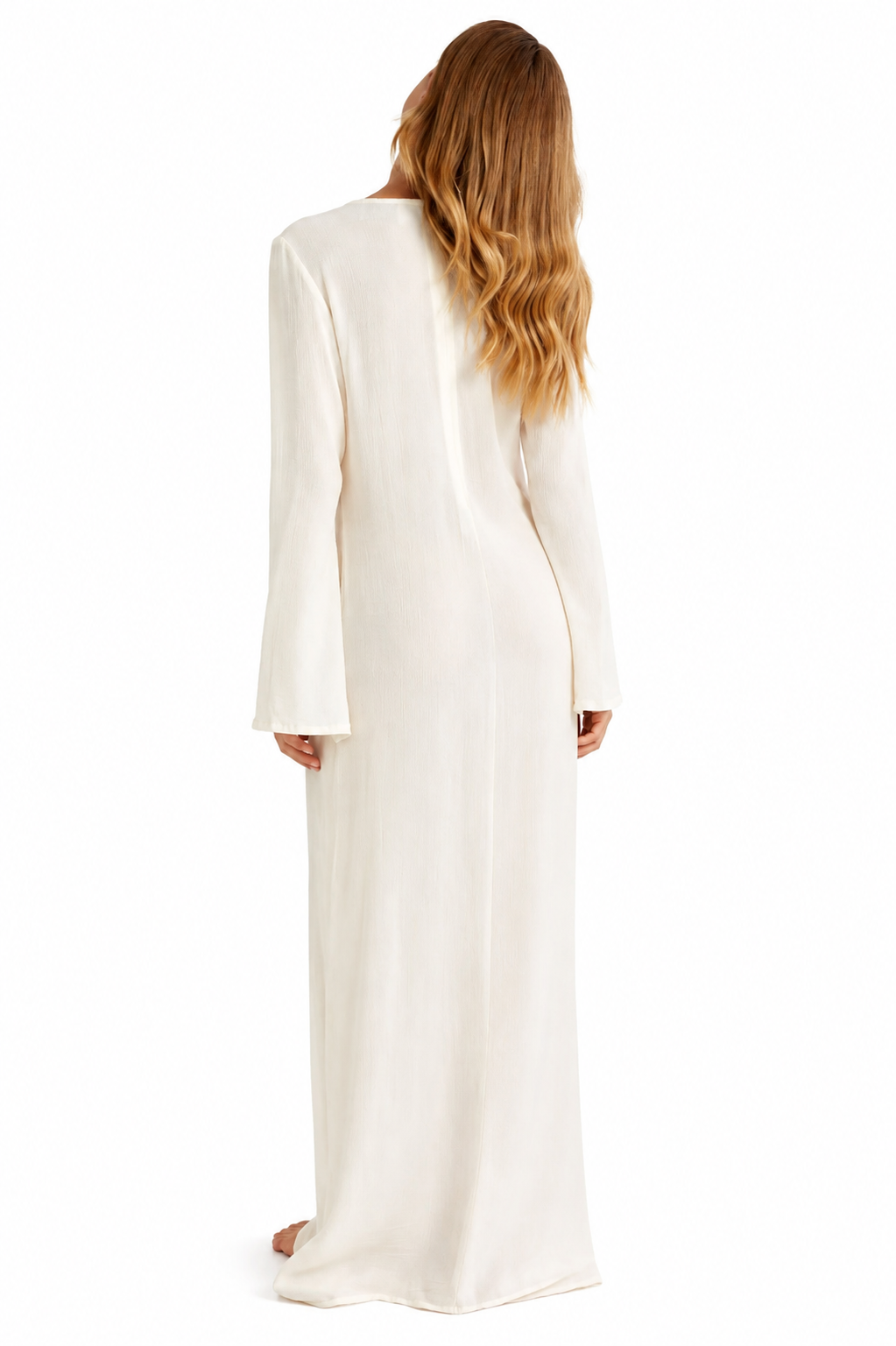 A woman viewed from behind wearing a long-sleeved, floor-length cream or off-white dress against a plain white background.