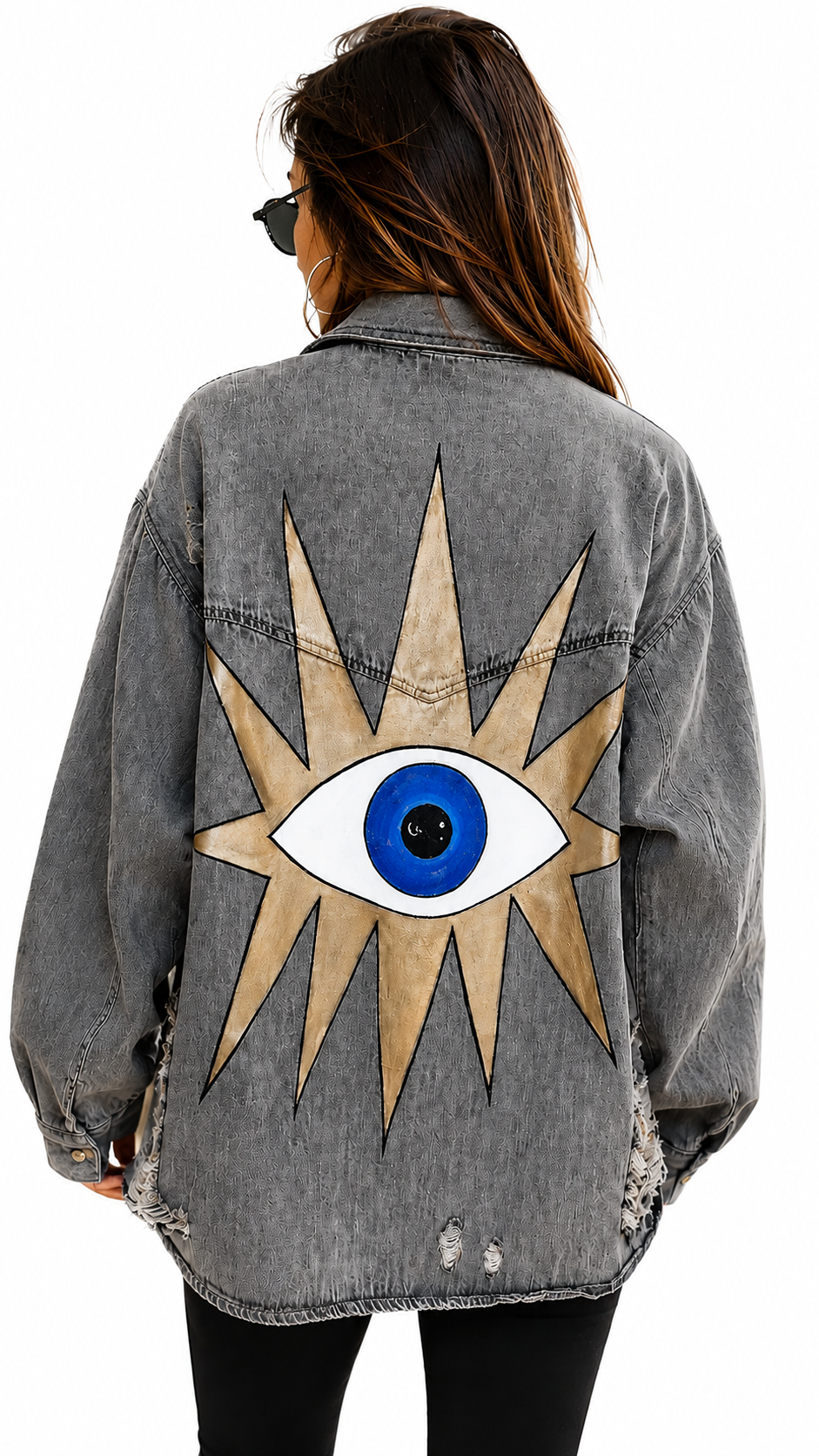A woman viewed from behind wearing a gray washed denim jacket with a large embroidered or printed eye and starburst design on the back. The jacket has distressed details and is paired with black pants against a plain white background.