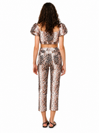 A model viewed from the back wearing a matching leopard-print two-piece set consisting of a short-sleeve crop top and cropped pants, paired with black sandals, on a solid white background.