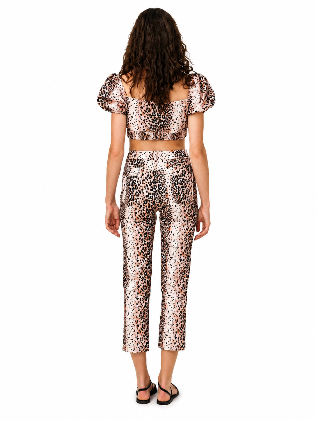 A model viewed from the back wearing a matching leopard-print two-piece set consisting of a short-sleeve crop top and cropped pants, paired with black sandals, on a solid white background.