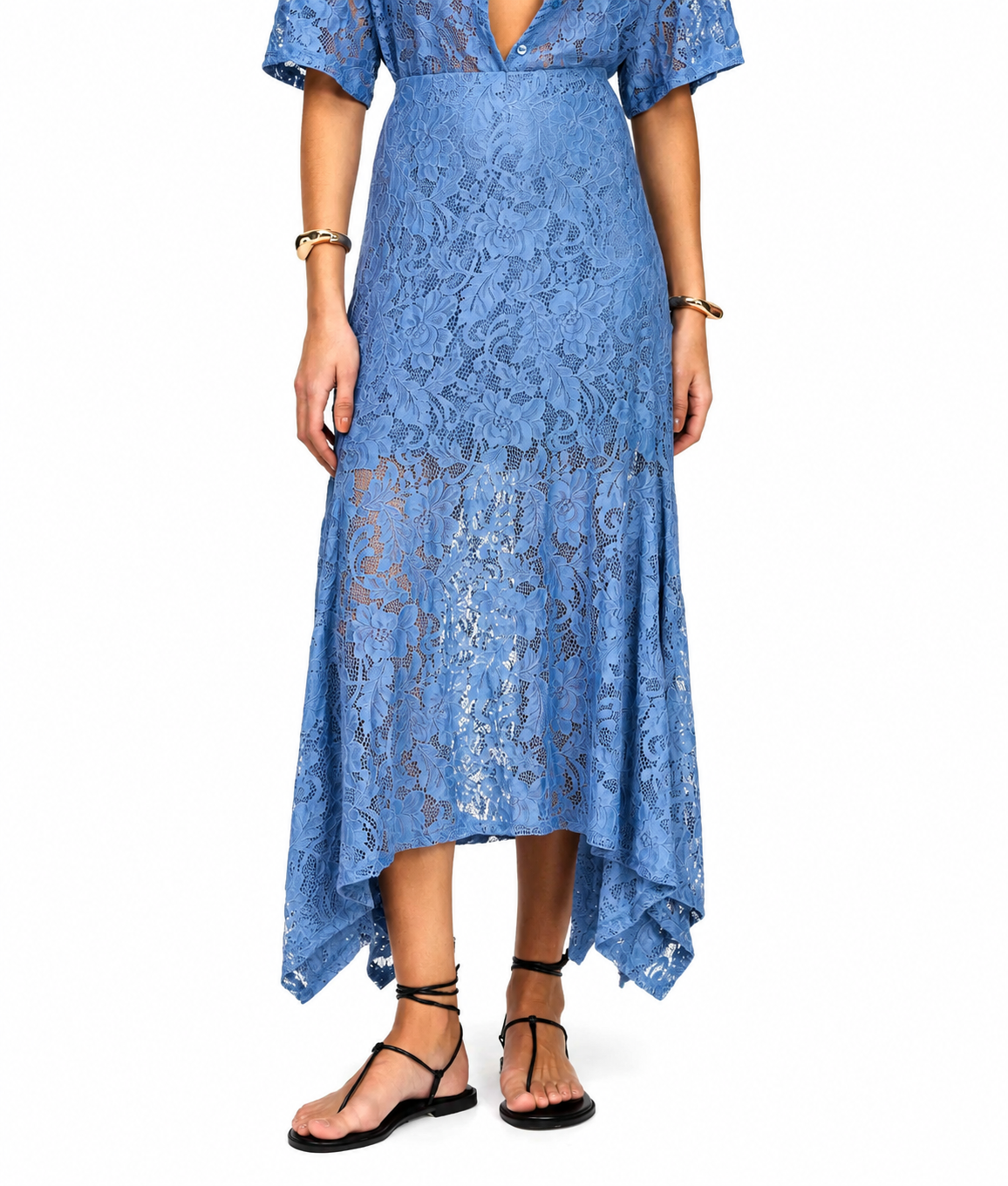 A woman modeling a blue lace midi dress with short flutter sleeves, a deep V-neckline, and an asymmetrical high-low hem, paired with black strappy flat sandals against a plain white background.