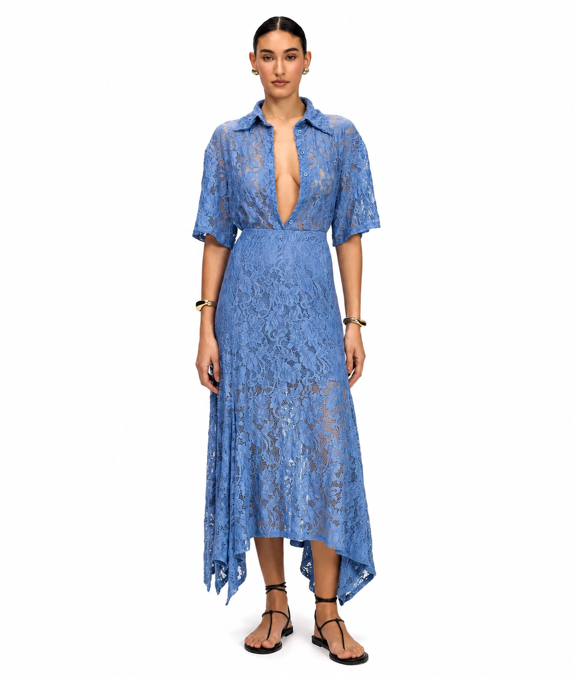 A model wearing a blue lace midi dress with short sleeves, a deep V-neckline, and an asymmetrical hem, paired with black strappy sandals against a plain white background.