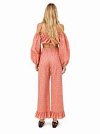 A woman viewed from the back wearing a matching off-the-shoulder crop top and wide-leg pants set in a peachy pink eyelet fabric, paired with black lace-up shoes, against a plain white background.