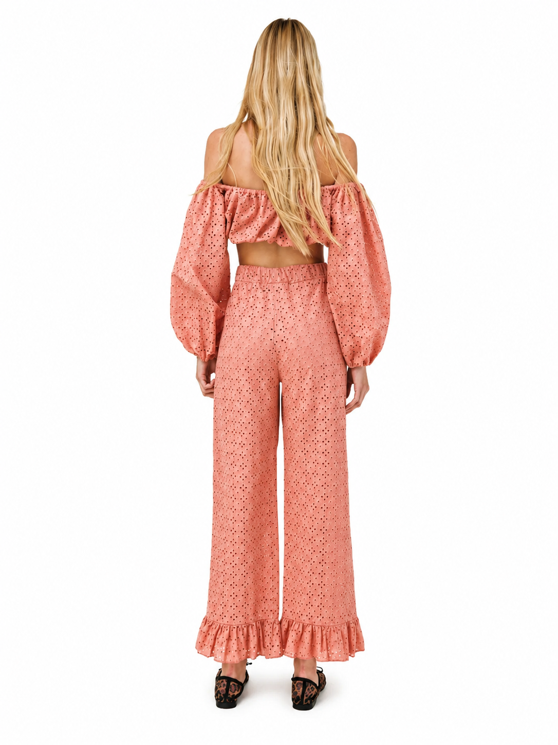 A woman viewed from the back wearing a matching off-the-shoulder crop top and wide-leg pants set in a peachy pink eyelet fabric, paired with black lace-up shoes, against a plain white background.