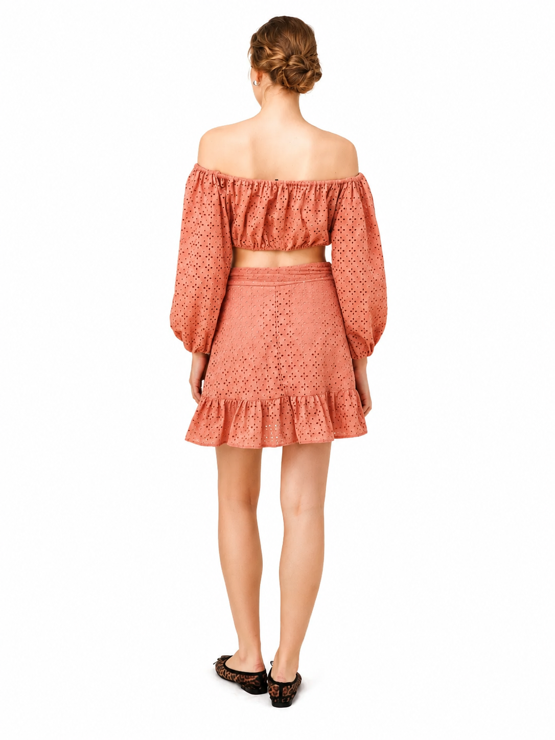 A woman shown from the back wearing a matching two-piece set consisting of an off-the-shoulder long-sleeve crop top and a high-waisted ruffled mini skirt, both in a textured terracotta orange fabric. She is wearing dark brown leopard print flats against a solid white background.