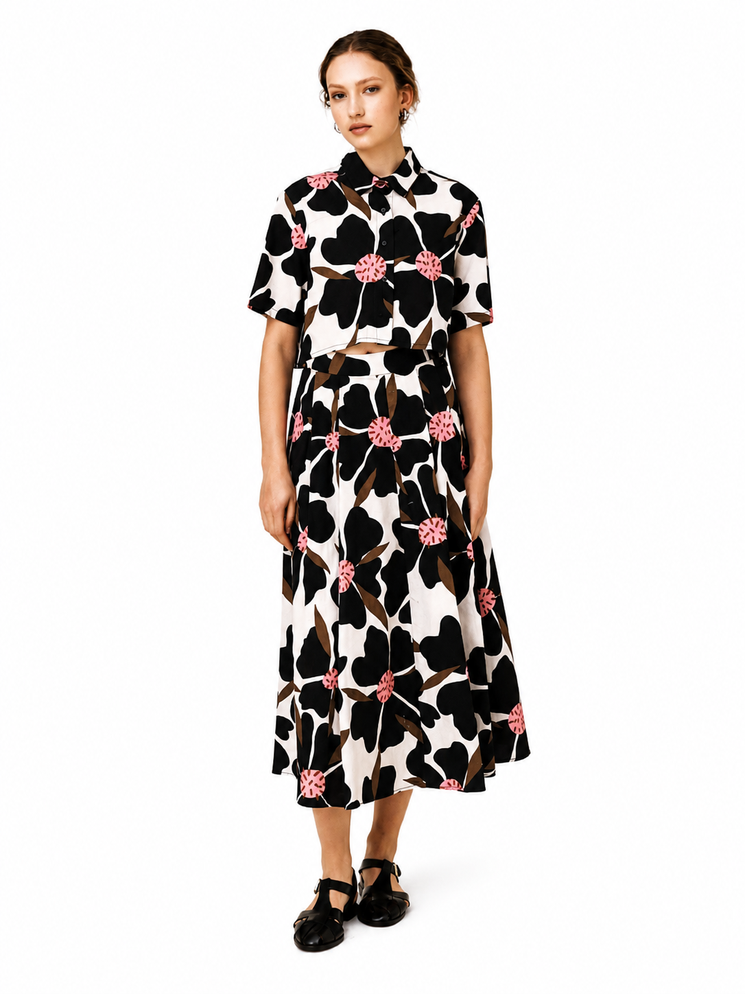 A woman modeling a matching short-sleeve collared shirt and midi skirt set with a bold black, white, and pink floral print, photographed against a solid white background.