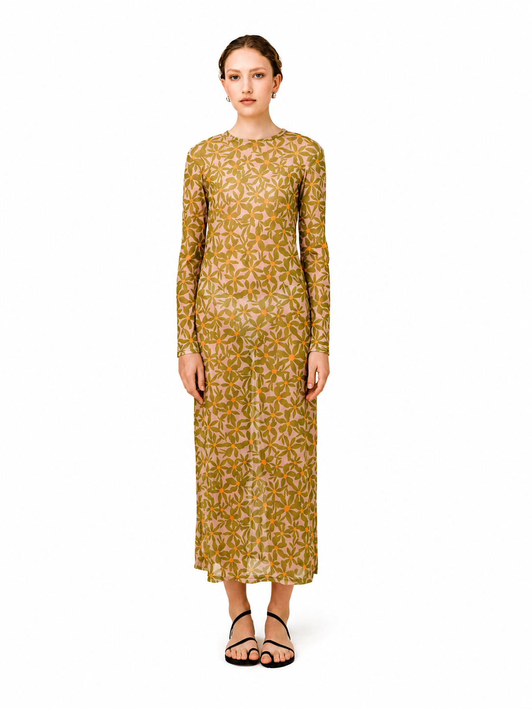 A woman modeling a long-sleeved midi dress with an all-over geometric floral pattern in mustard yellow and olive green, paired with black strappy sandals, against a plain white background.