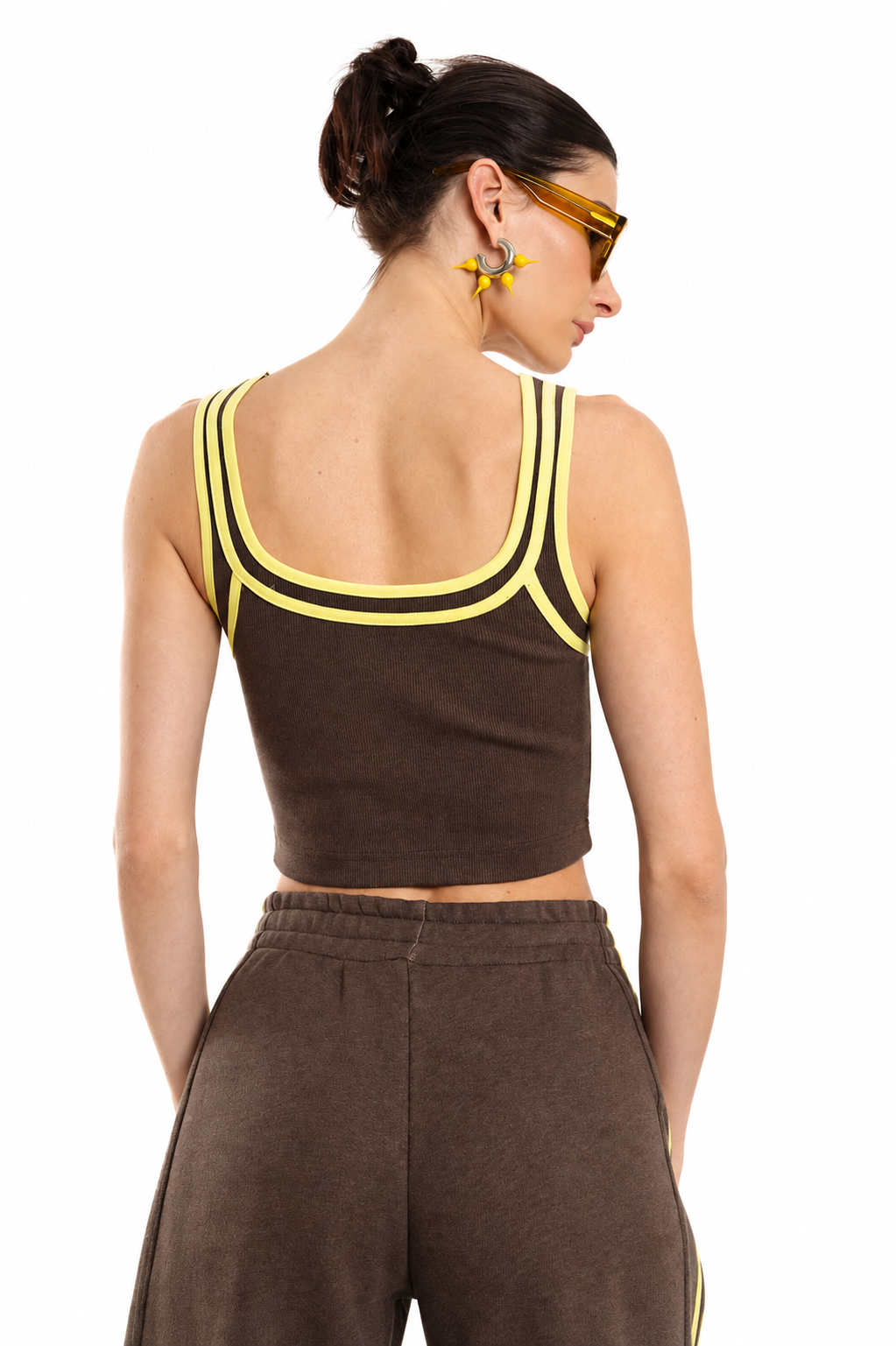 A model shown from the back wearing a brown cropped tank top with yellow trim and matching brown pants, against a plain white background.