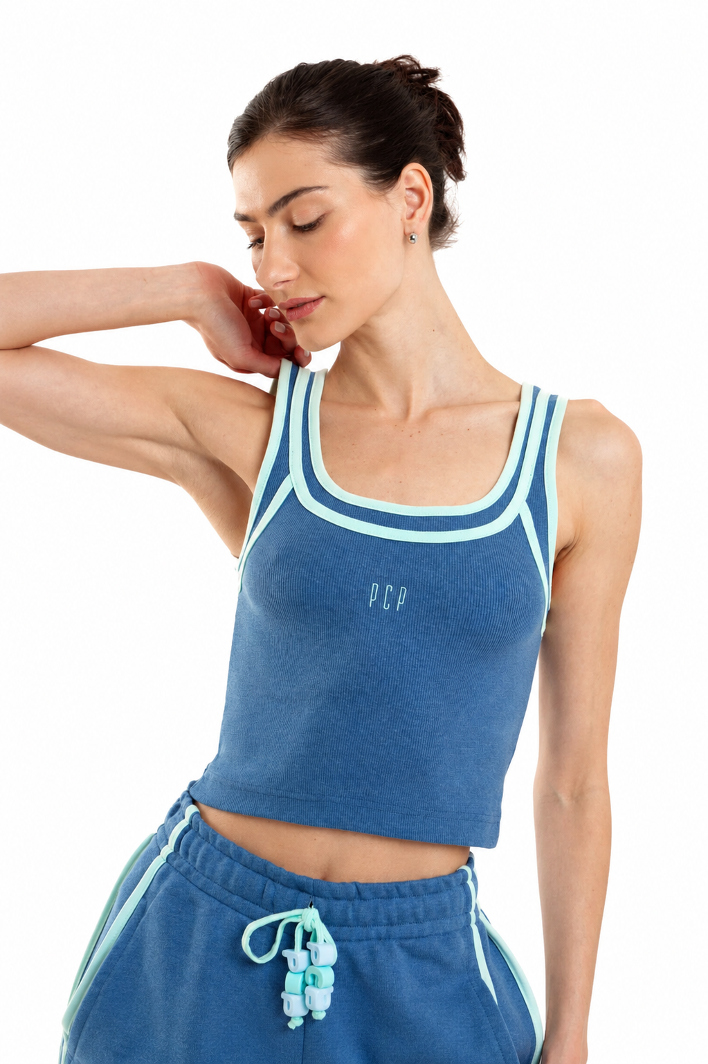 A woman modeling a blue cropped tank top with light blue trim and matching blue sweatpants against a white background.