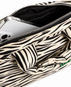 Close-up of a zebra-print fabric bag with an open zipper, showing a silver smartphone inside, on a white background.