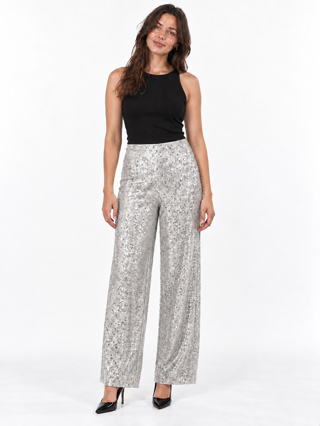 A woman modeling a pair of high-waisted, wide-leg pants with a silver and black abstract pattern, paired with a black sleeveless top and black heels, against a plain white studio background.