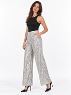 A woman modeling high-waisted, wide-leg silver sequin pants paired with a black sleeveless top and black pointed-toe heels, set against a plain white studio background.