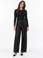 A woman modeling a black long-sleeve top and black wide-leg sequined pants with black pointed-toe heels, standing against a plain white studio background.