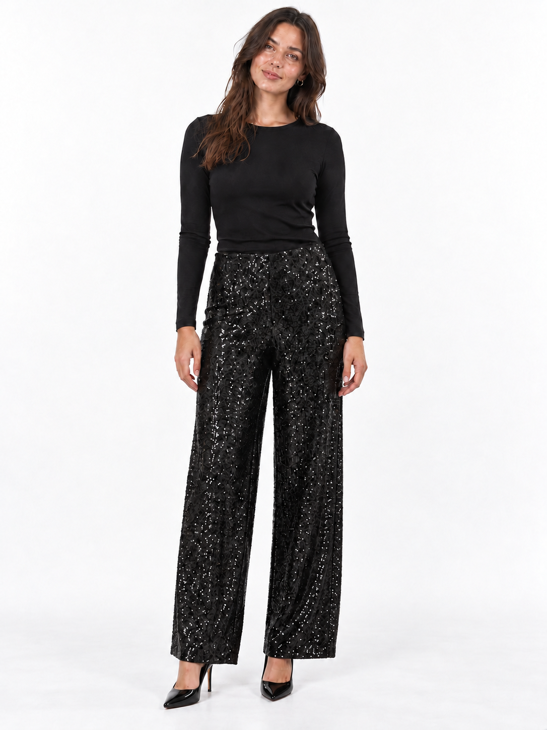 A woman modeling a black long-sleeve top and black wide-leg sequined pants with black pointed-toe heels, standing against a plain white studio background.