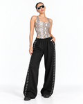 A model wearing a snakeskin-patterned bodysuit and black wide-leg pants with white lettering down the sides, posing against a white studio background.