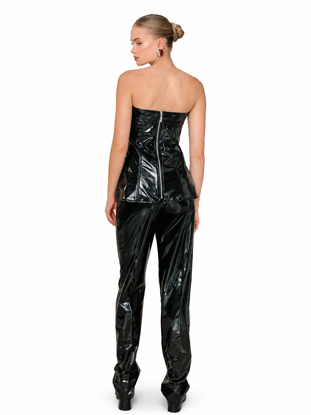 A model shown from the back wearing a glossy black strapless corset top and matching high-waisted patent pants against a plain white background.