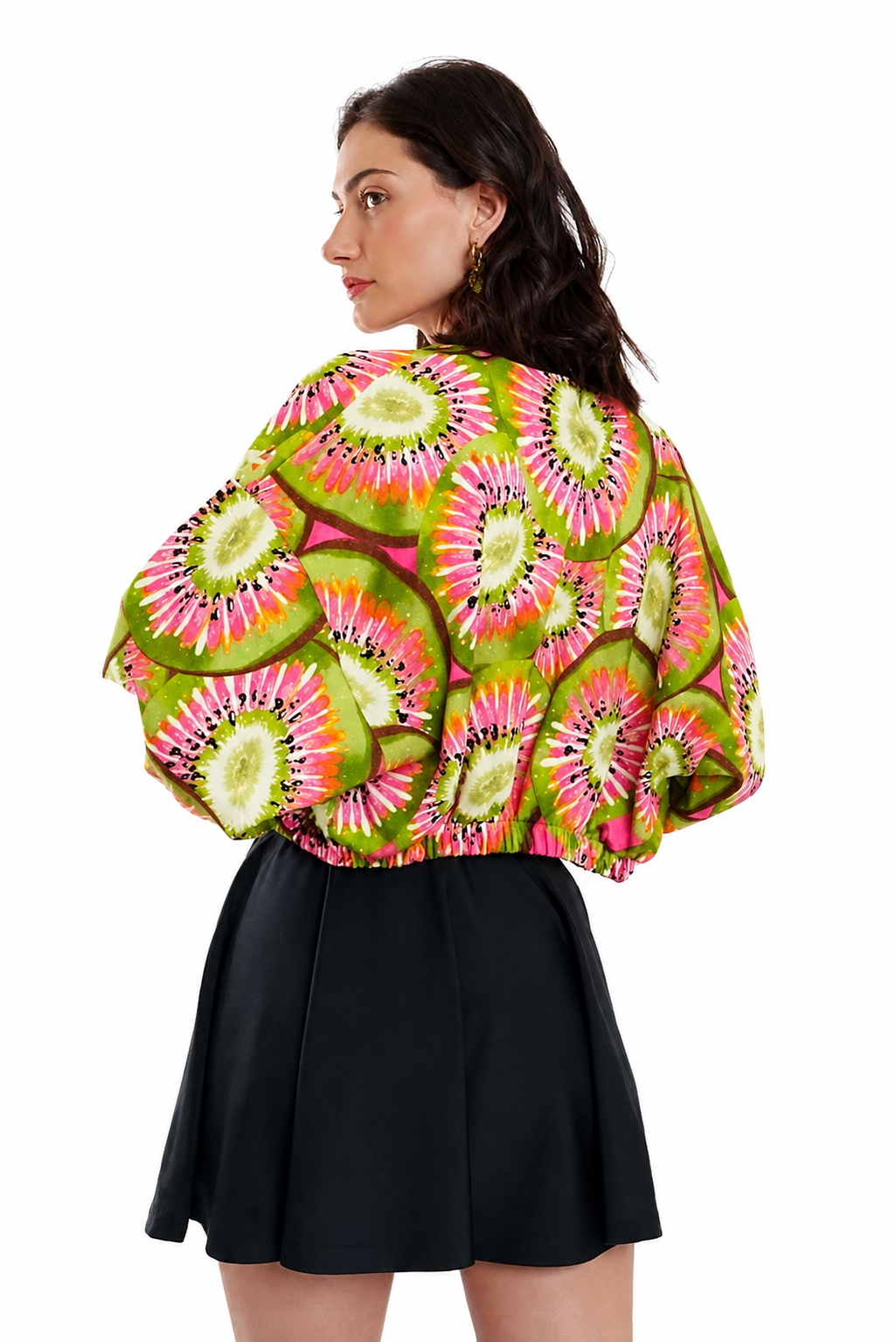 A woman shown from the back wearing a vibrant green, pink, and yellow kiwi-patterned blouse with a black pleated skirt, set against a plain white background.