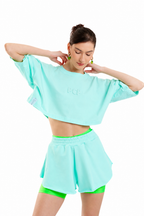 A model wearing a mint green cropped t-shirt and matching shorts with neon green inner shorts, posed against a solid white background.