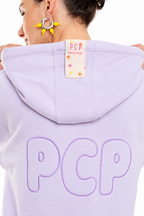 A close-up back view of a person wearing a light lavender hoodie with large outlined 'PCP' lettering across the back and a small sewn-in label at the hood. The person is shown from the back with hands holding the shoulders, against a plain white background.