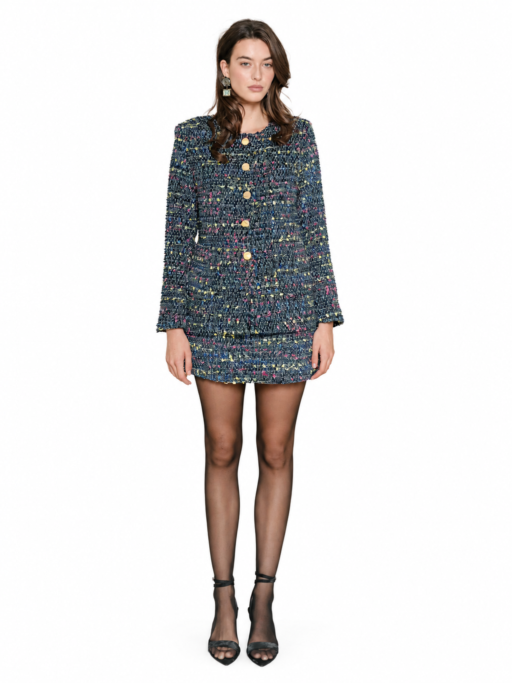 A model wearing a dark blue tweed jacket with gold buttons and tweek skirt, paired with sheer black tights and black high-heeled sandals, against a plain white background.