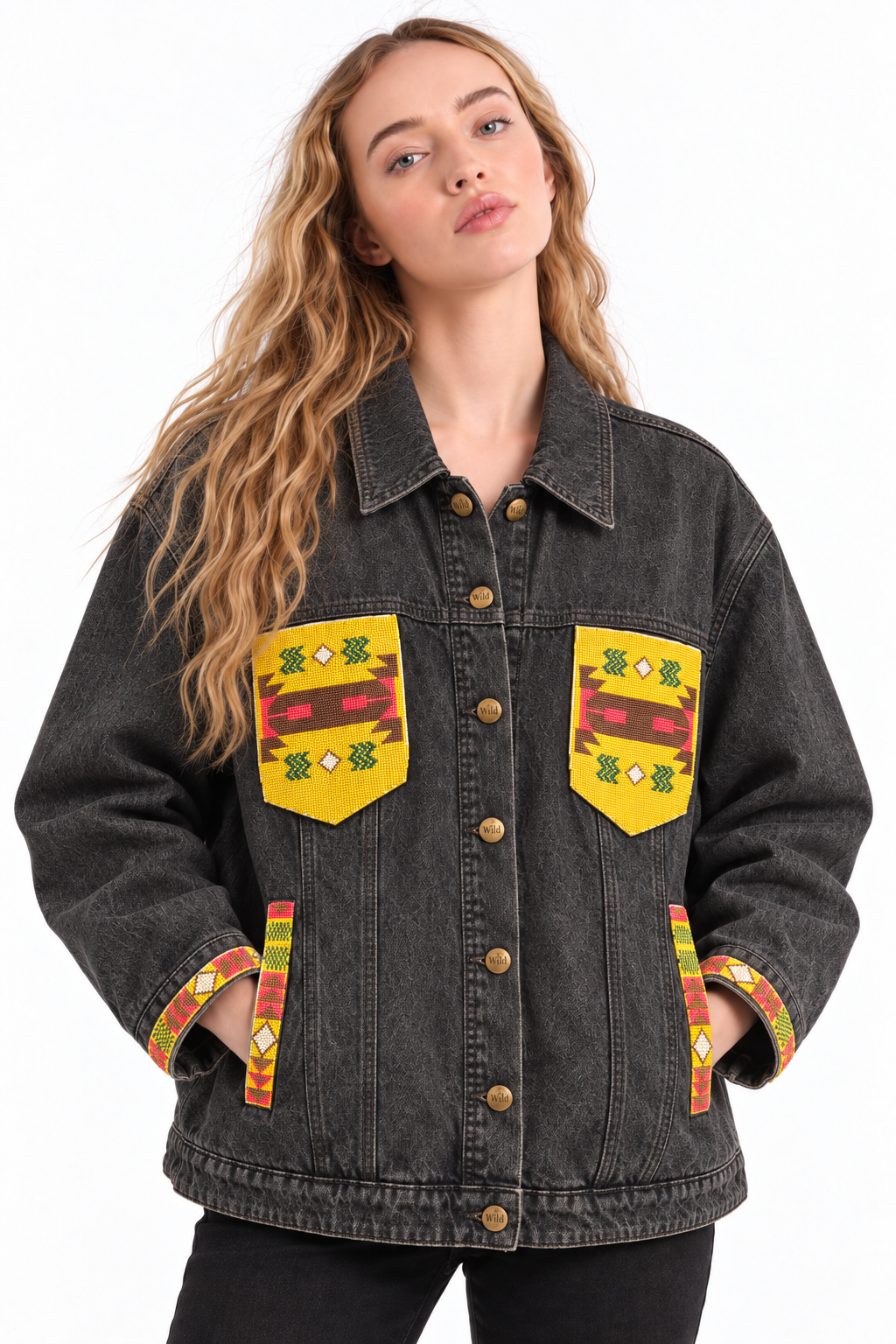 A woman wearing a dark gray washed denim jacket with yellow, red, and green geometric patterned chest and pocket patches, shown against a plain white background.