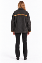 A model viewed from the back wearing a washed black denim jacket with a colorful patterned horizontal stripe across the upper back and black pants, set against a plain white studio background.