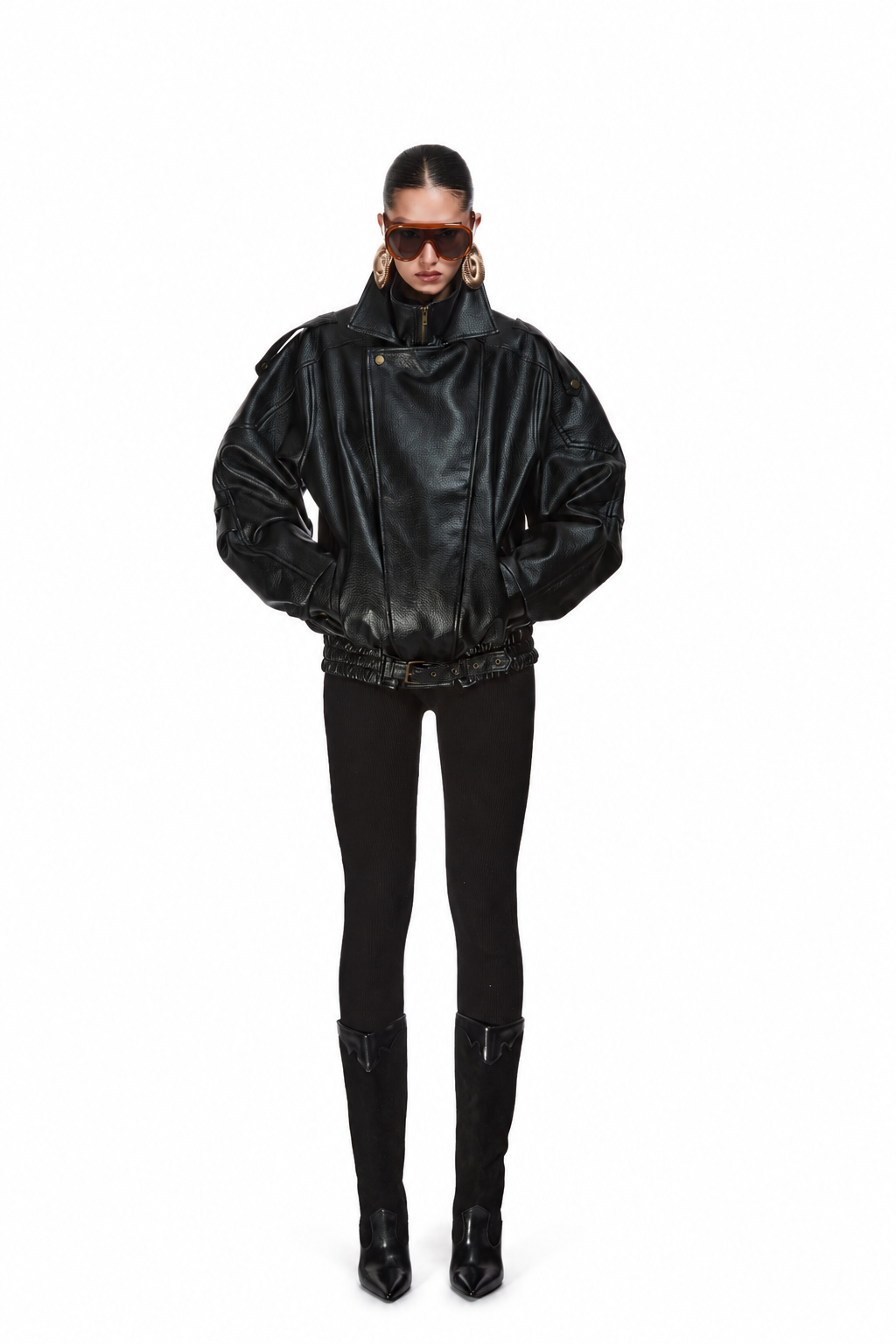 A model wearing a black leather bomber jacket with dramatic puffed shoulders, black pants, and black knee-high boots, photographed against a solid white background.