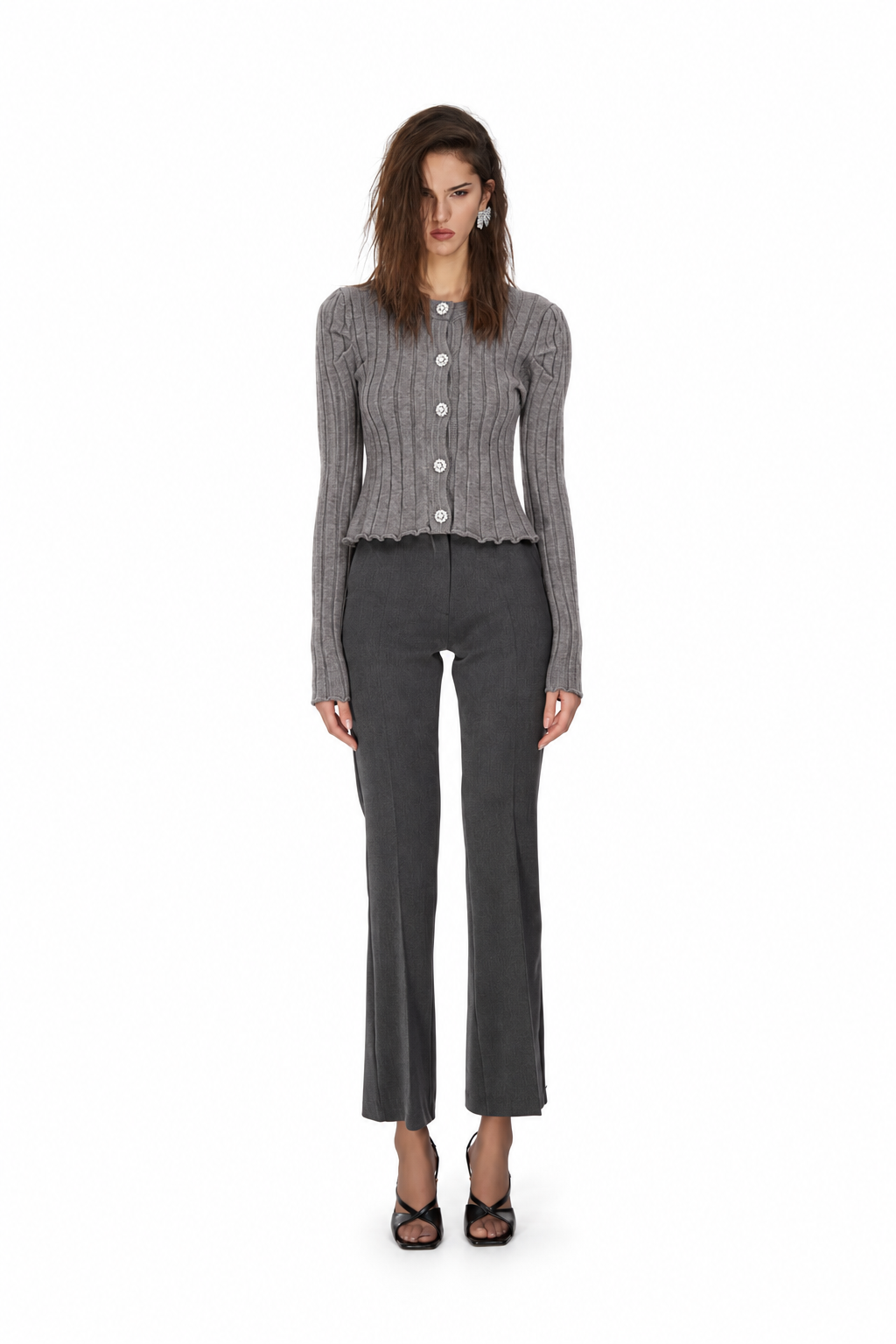 A model stands against a solid white background wearing a gray ribbed button-up cardigan, dark gray cropped flare pants, and black strappy heels.