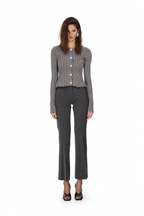 A model stands against a solid white background wearing a gray ribbed button-up cardigan, dark gray cropped flare pants, and black strappy heels.