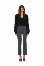A model stands against a plain white background wearing a black fuzzy cropped jacket, dark gray cropped trousers, and black strappy heels.