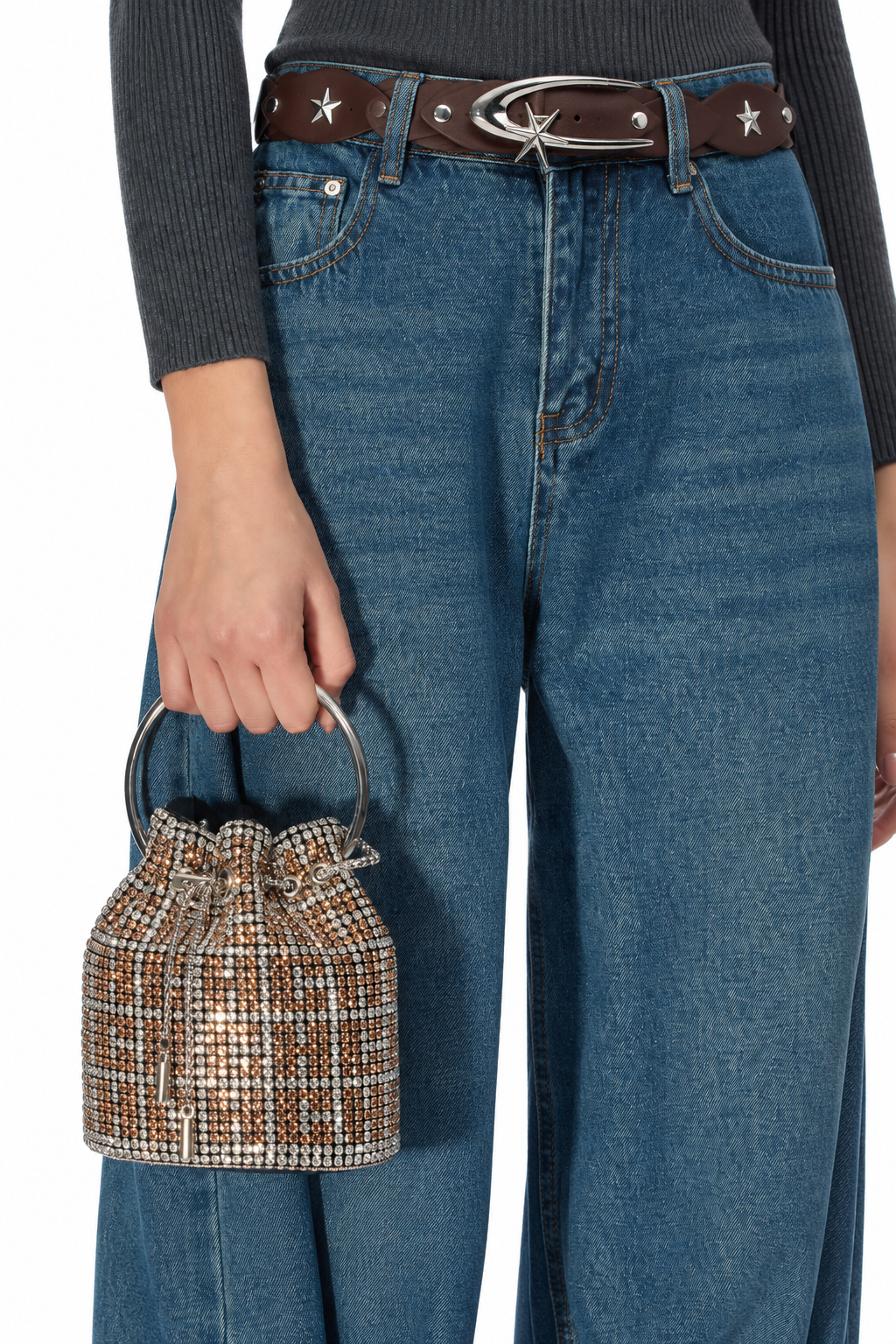 A person wearing blue wide-leg jeans, a dark gray ribbed sweater, a brown belt with silver star details, and holding a small tweed bucket bag with a silver handle.