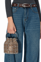 A person wearing blue wide-leg jeans, a dark gray ribbed sweater, a brown belt with silver star details, and holding a small tweed bucket bag with a silver handle.