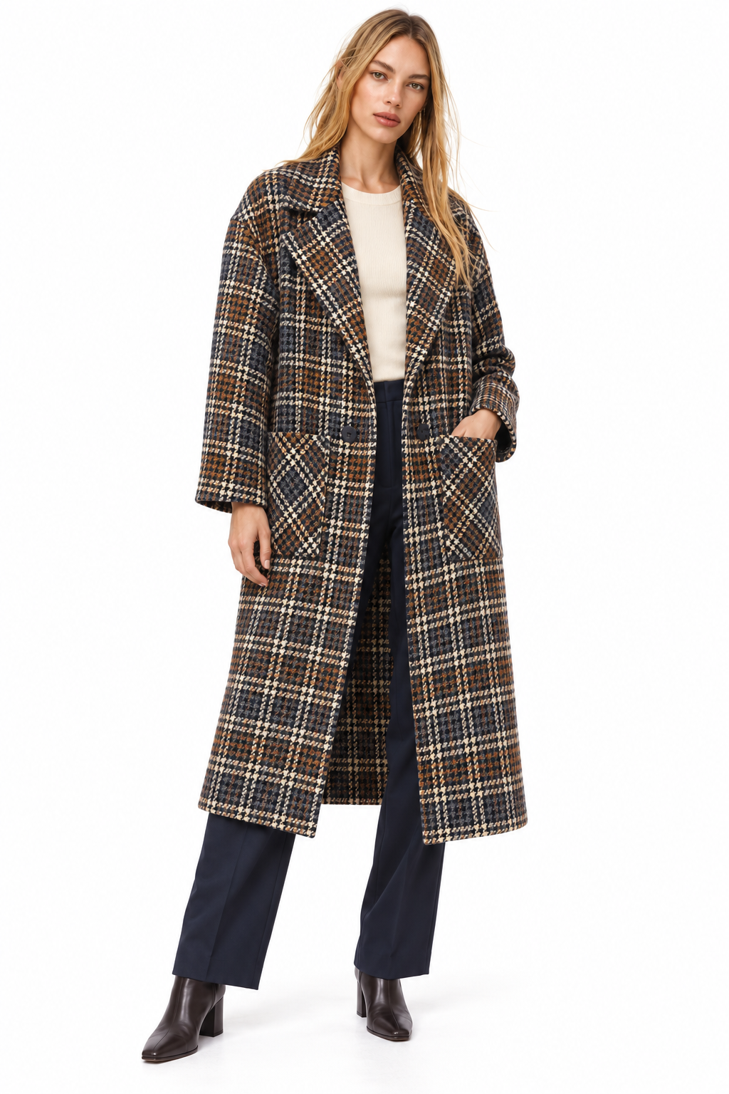 A woman modeling a long plaid coat over a cream top, navy wide-leg pants, and dark brown ankle boots, photographed against a plain white studio background.