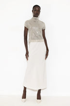 A model wearing a high-neck, short-sleeved dress featuring a shimmering silver sequined bodice and a solid white skirt, standing against a plain white studio background.