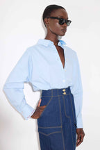 Person wearing a light blue shirt and dark blue denim pants with sunglasses on a white background