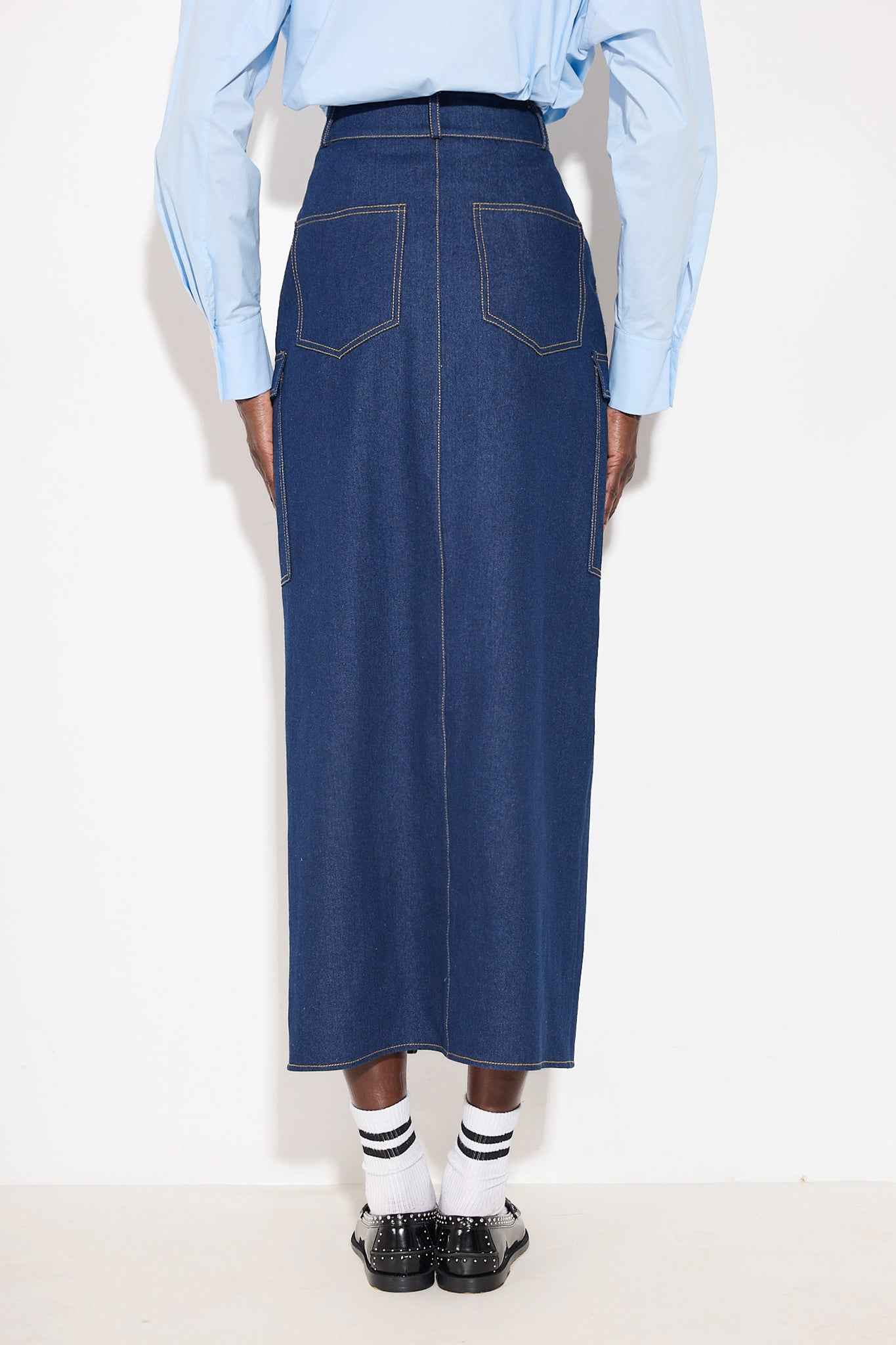 Person wearing a blue denim skirt with a light blue shirt on a white background