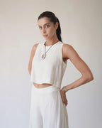 Woman wearing a white sleeveless top and pants against a plain background