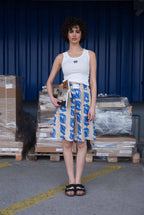 Woman holding a magazine in front of stacked boxes and pallets against a blue wall.