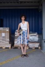 Person standing in an industrial setting with blue curtains and stacked pallets.