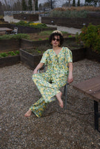 Woman in a green and yellow patterned outfit sitting in a garden setting.