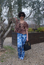 Person wearing a leopard print top and blue patterned pants standing outdoors with trees in the background.