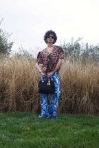 Person wearing a leopard print top and blue patterned pants standing in a grassy field with tall brown grass.