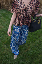Person wearing a leopard print top and blue patterned pants, holding a black handbag on grass.